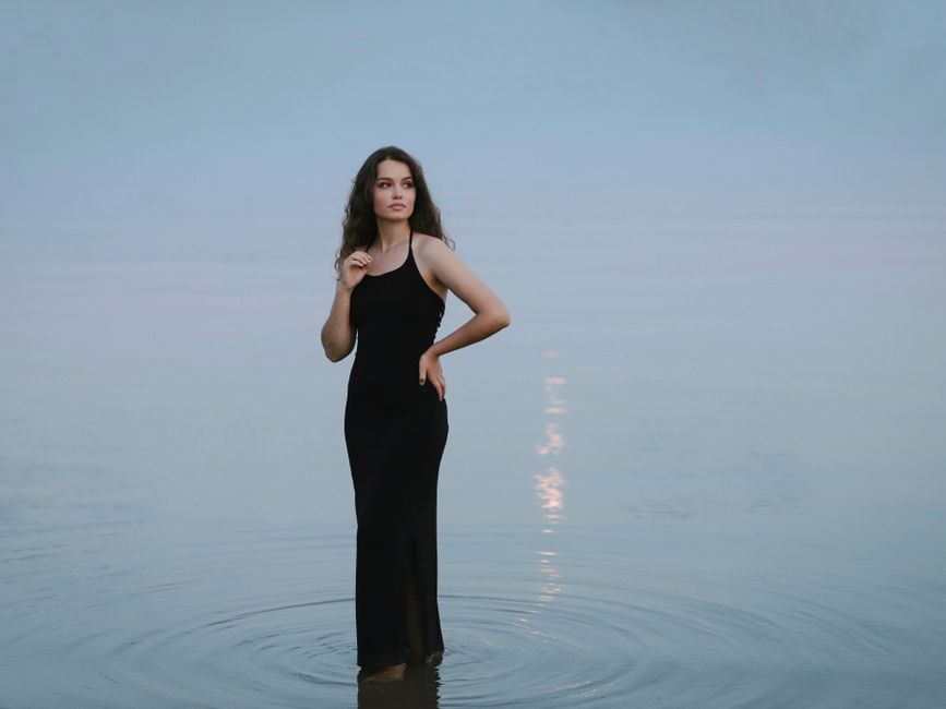 A young woman in a black dress standing in water during sunset in Ukraine.