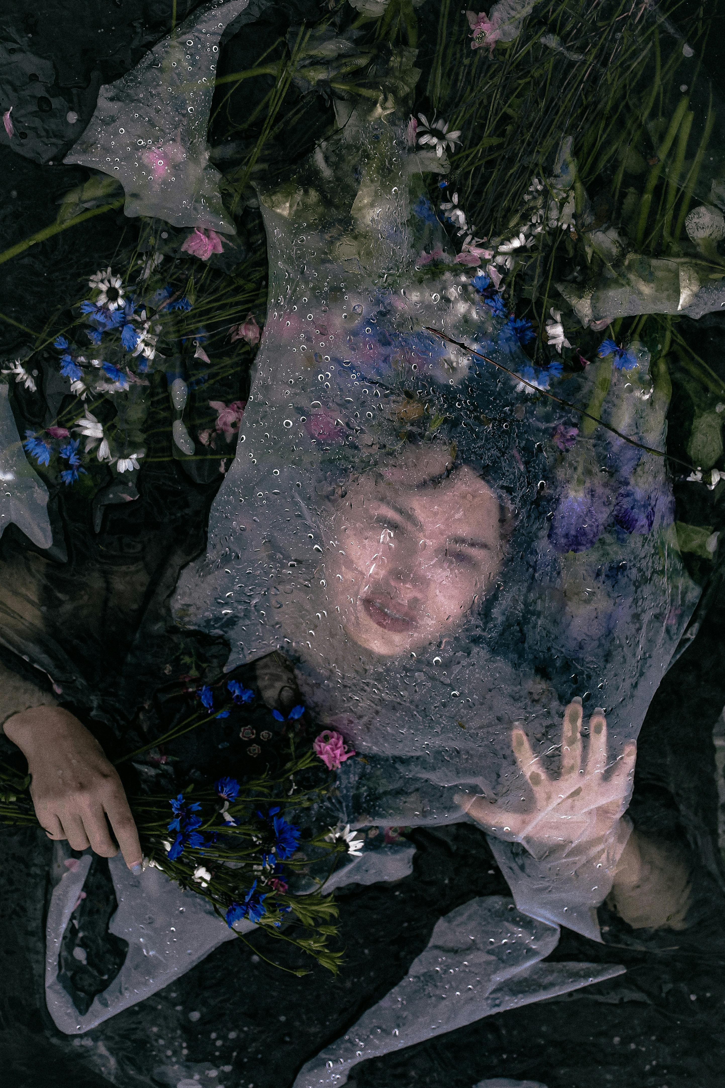 Artistic portrait of a woman obscured by a net, surrounded by flowers underwater.
