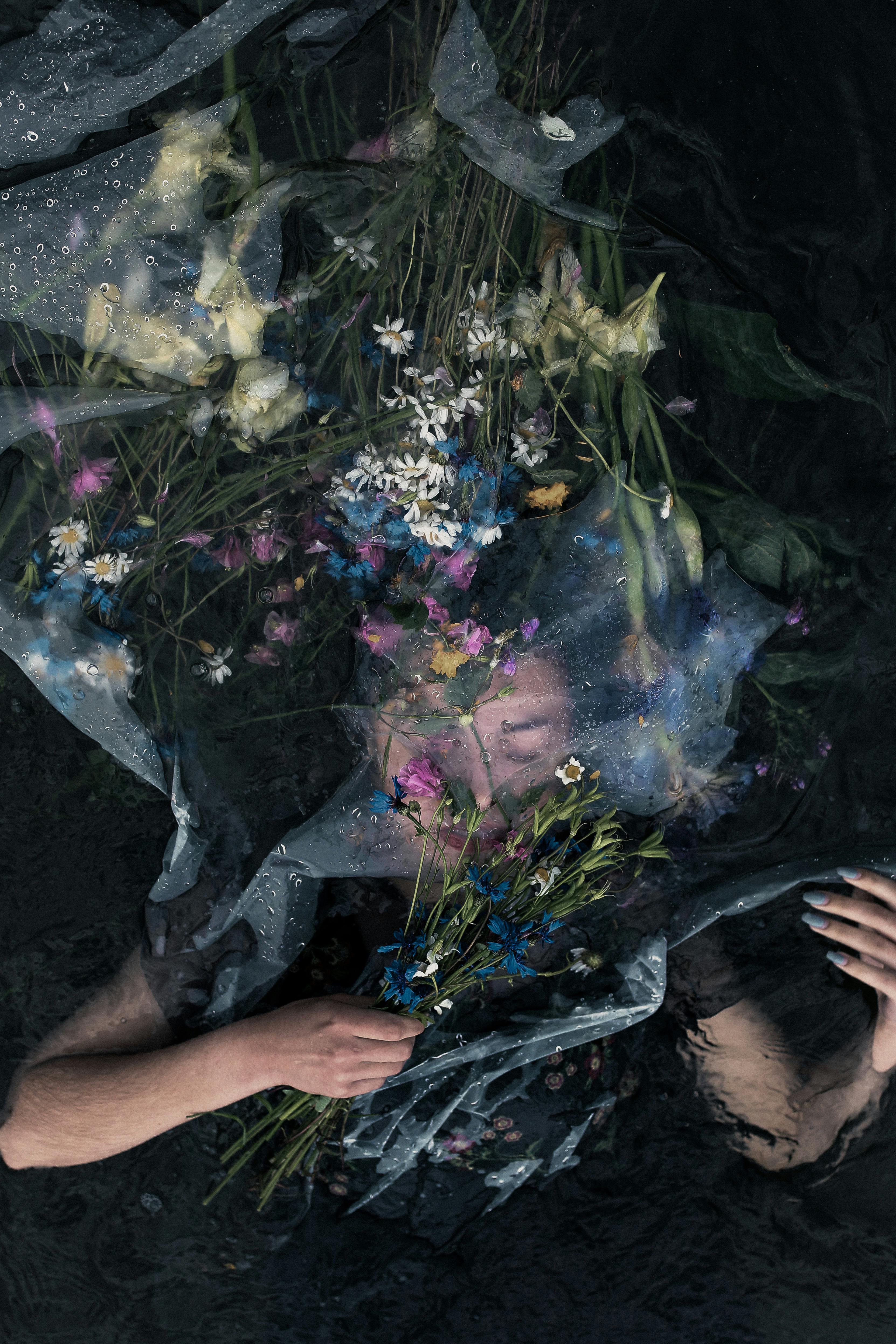 A woman submerged with flowers creates a dreamy, artistic composition in dark waters.