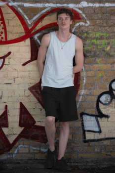 Casual young man in tank top and shorts standing by graffiti wall in Berlin. Urban summer vibe.