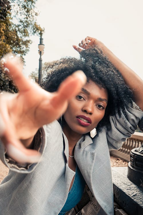 Young Fashionable Woman Posing Outside and Reaching Her Hand Toward the Camera 