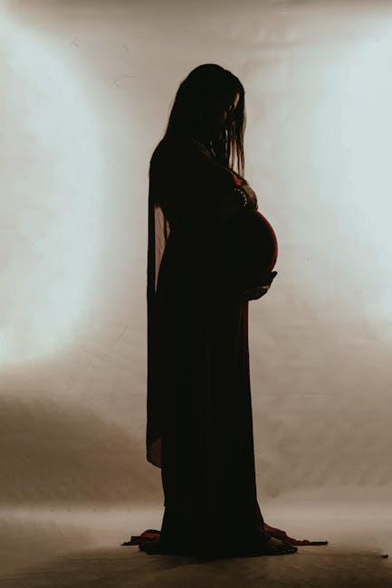 Artistic silhouette of a pregnant woman in a dress posing gracefully in a studio setting.