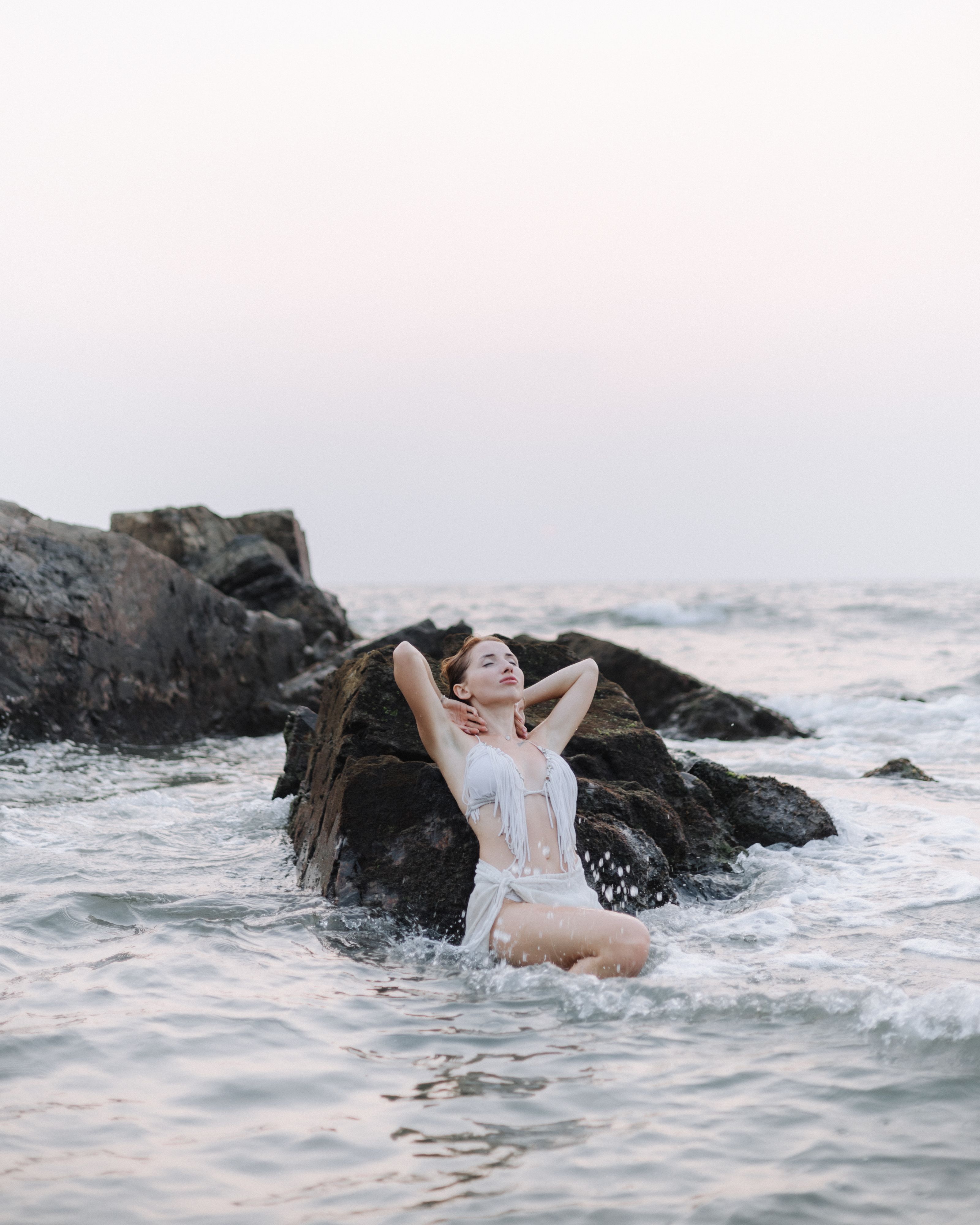 Uma mulher em um traje de banho branco desfruta de um momento sereno à beira-mar em um dia ensolarado.