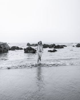 Black and white photo of a woman standing on a rocky beach, exuding tranquility.