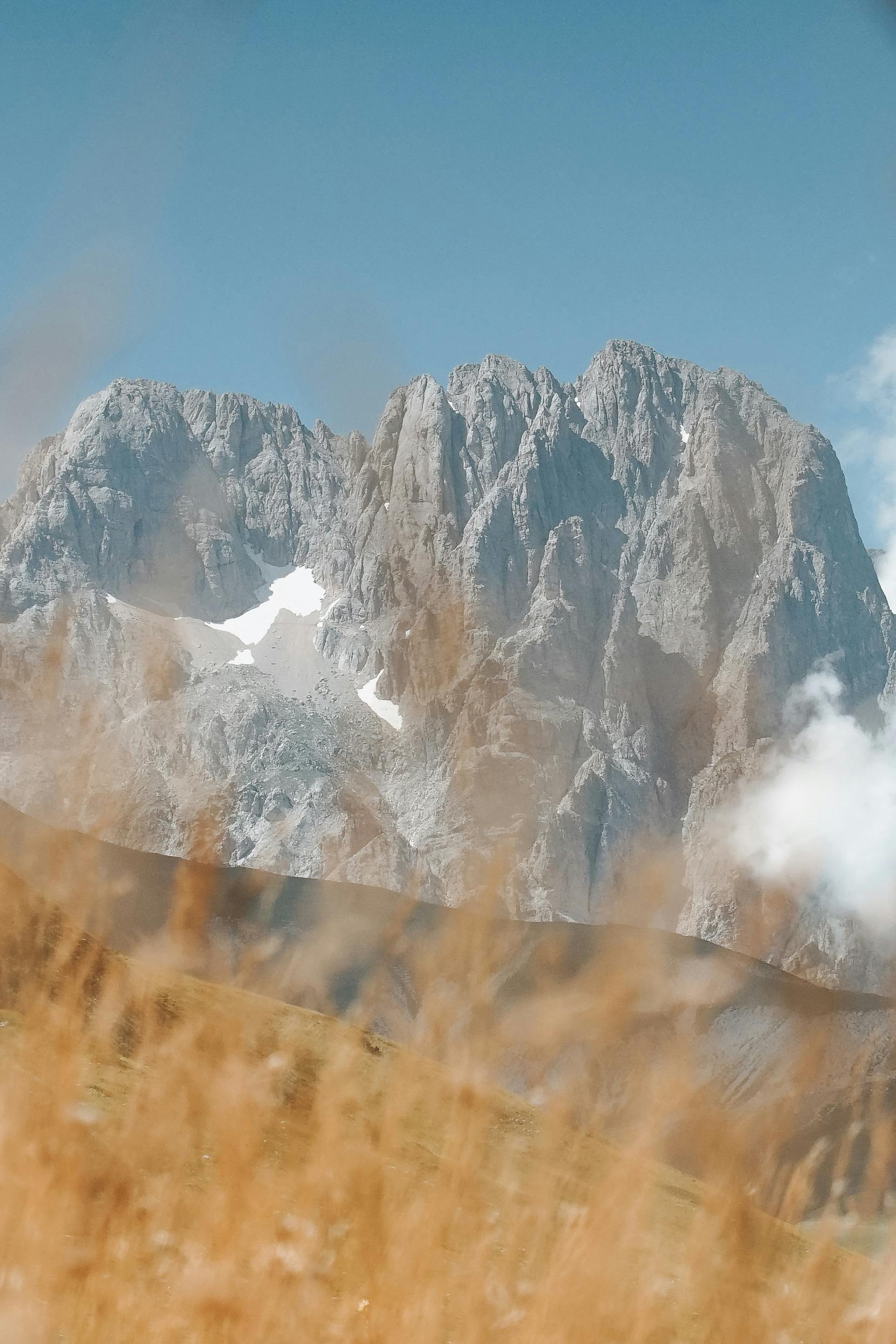A breathtaking view of a rocky mountain peak surrounded by tall grass under a clear blue sky.