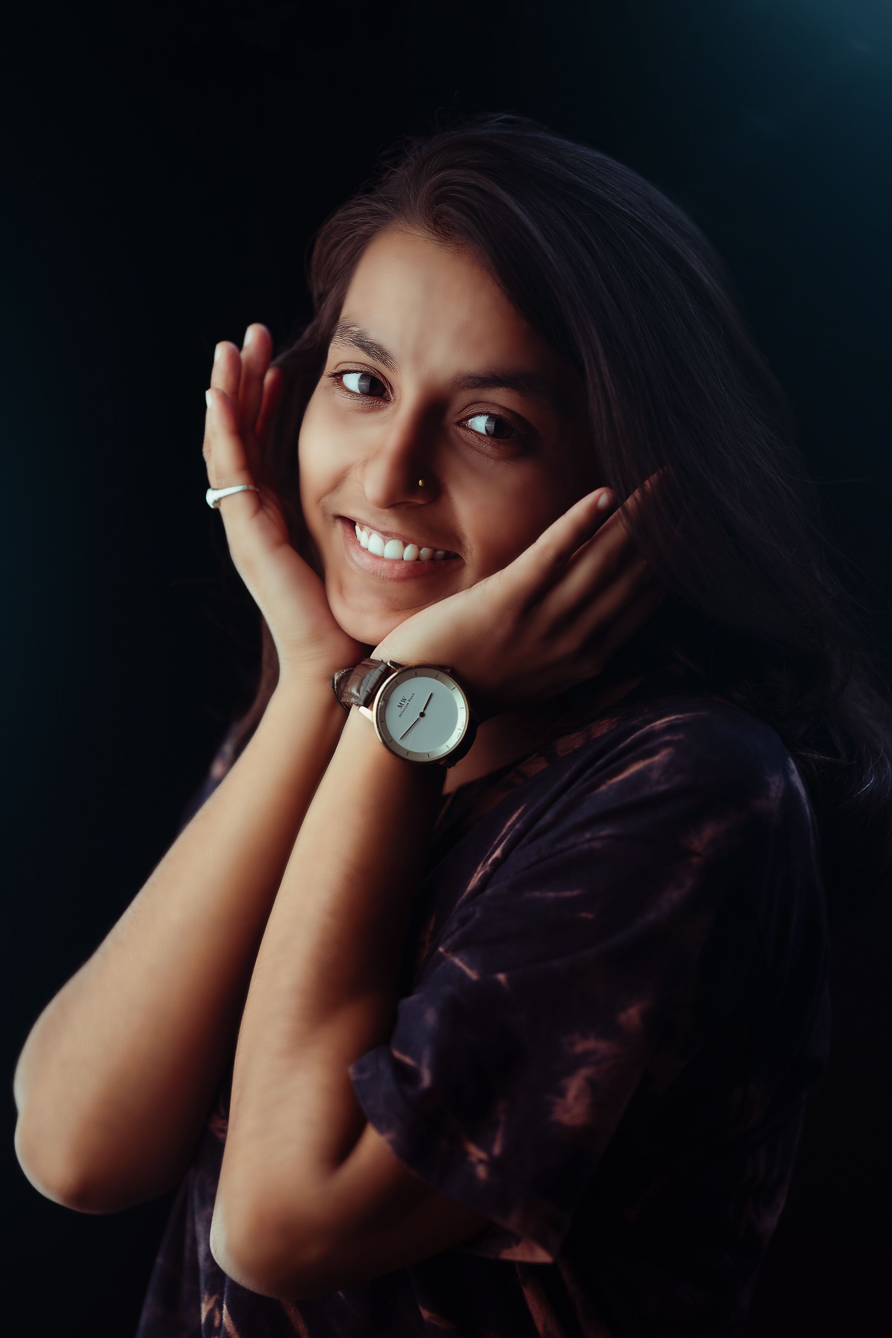 A vibrant portrait of a smiling young woman posing elegantly with hands to her face, showcasing a wristwatch.