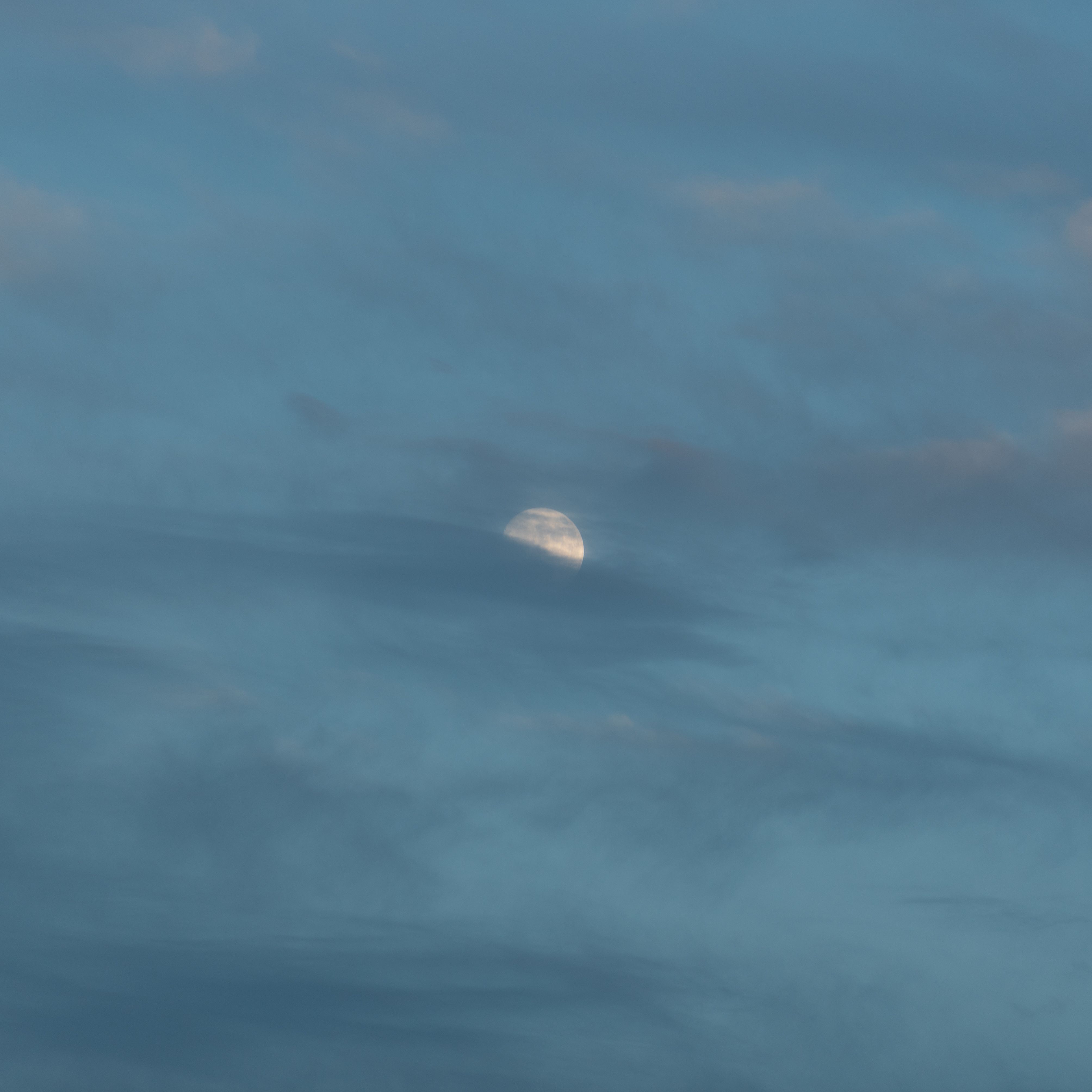 A peaceful scene of the moon partially obscured by clouds during twilight, creating a calming atmosphere.