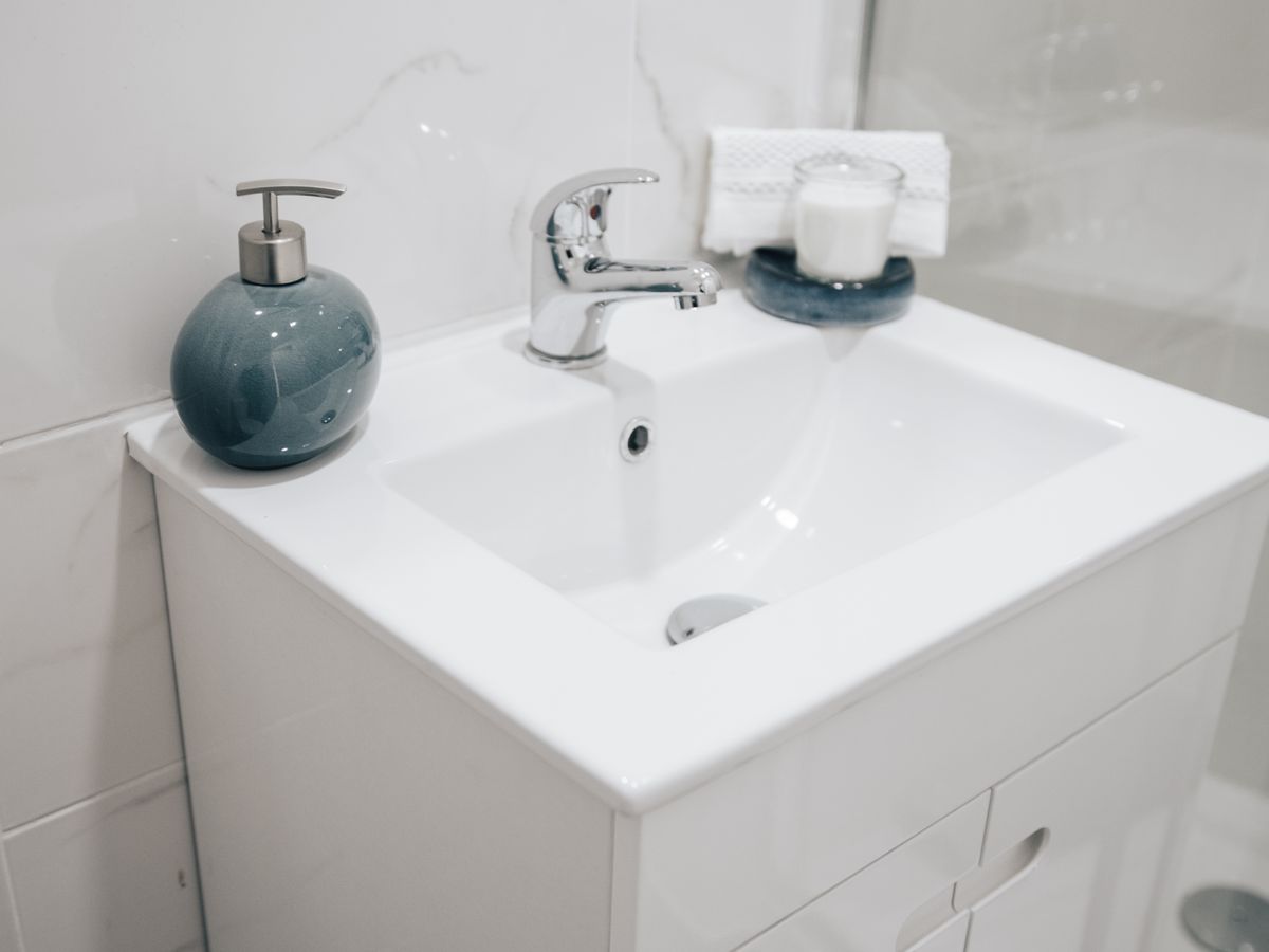 A bathroom sink with a chrome faucet, soap dispenser and towel.