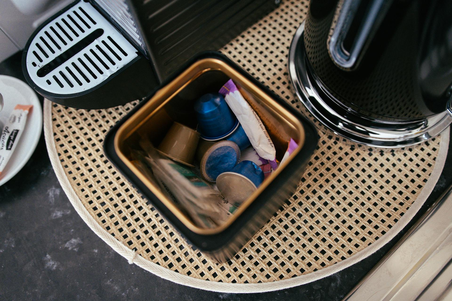 Overhead view of coffee pods stored next to a coffee machine and kettle in a kitchen setting.