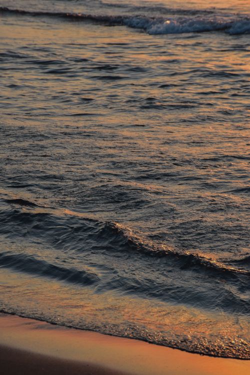 Free Gentle waves wash over Cebeci Beach during a stunning sunset, creating a peaceful atmosphere. Stock Photo