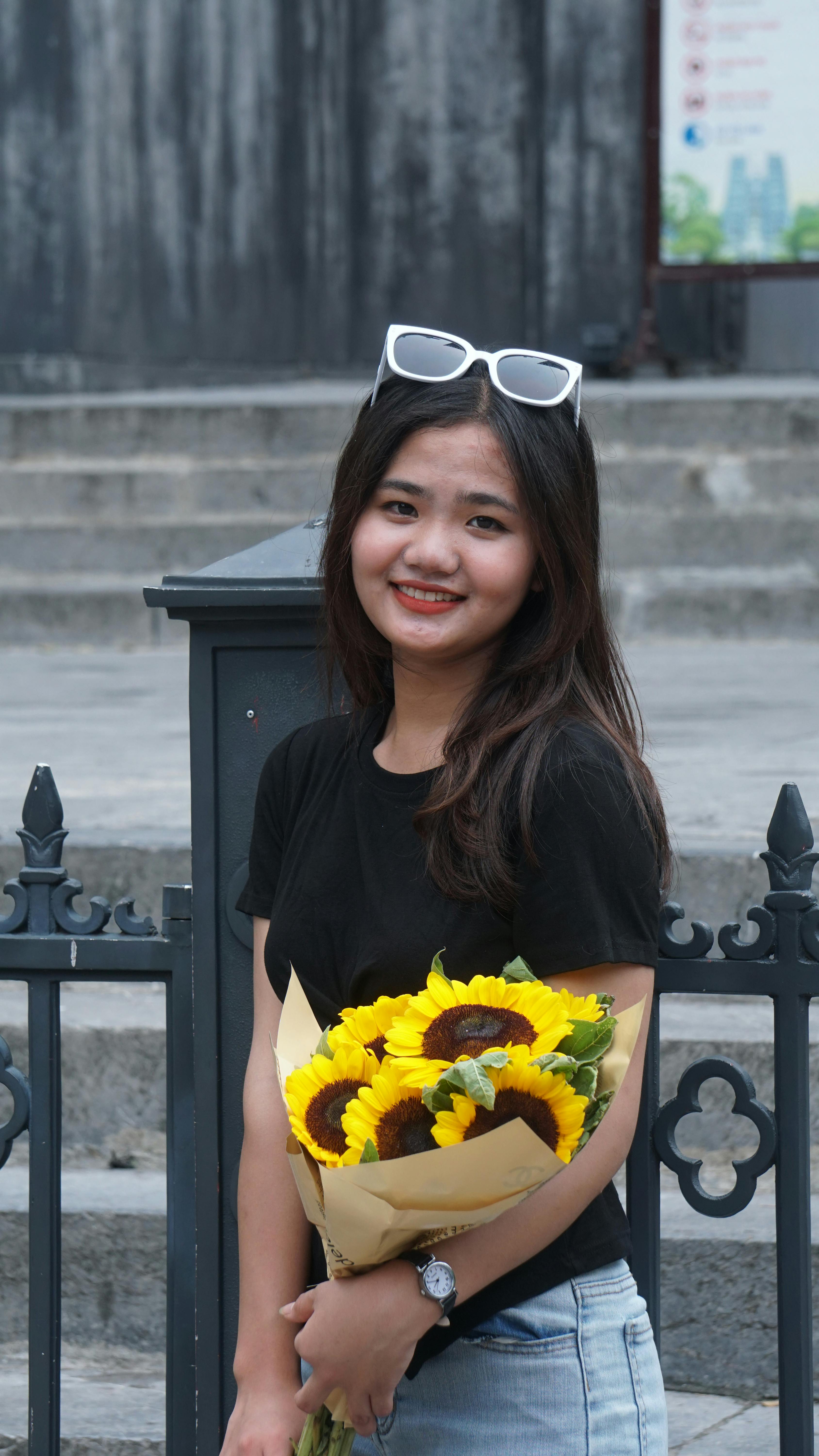 A smiling young woman outdoors holding a bouquet of vibrant sunflowers.