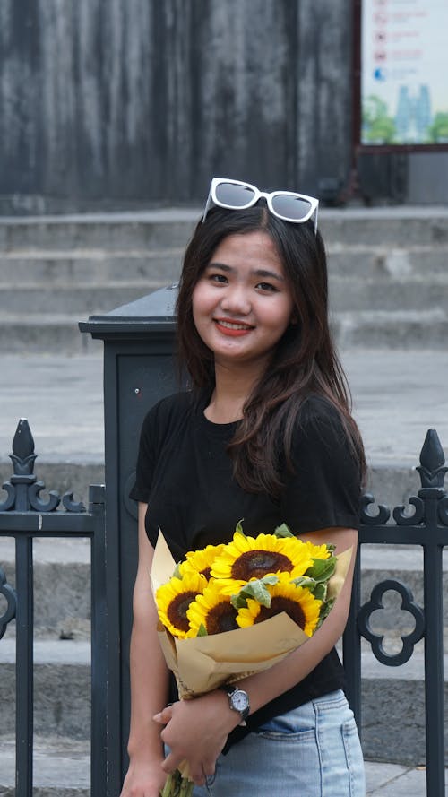A Young Woman with a Bunch of Sunflowers Standing Outside and Smiling 