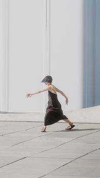 A woman elegantly dancing on pavement in a black dress, captured in motion.