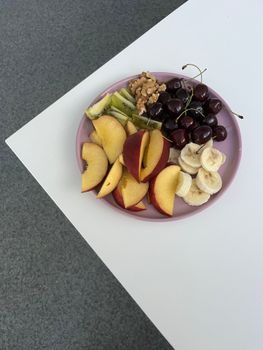 Colorful fruit platter featuring cherries, peaches, bananas, and walnuts on pink plate.