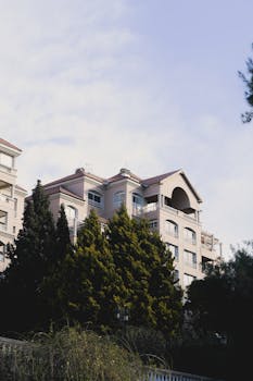 Elegant apartment building facade with trees against a blue sky in an urban setting.