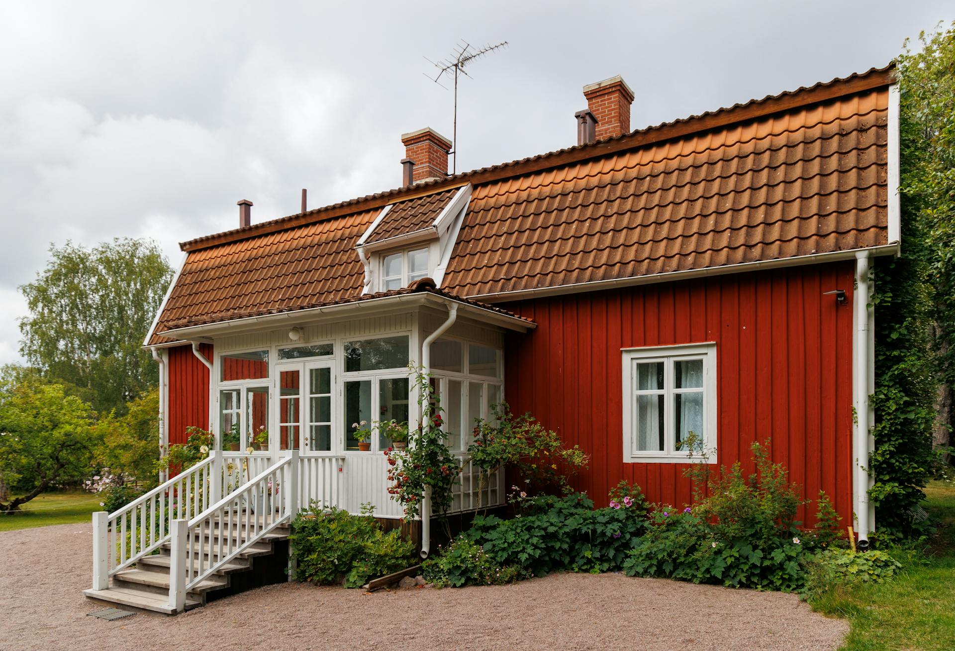 A picturesque rural red wooden house with white trim and a tailed gable roof.