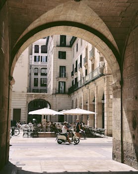 Cafe seating under archways in Alicante, Spain with a person on a scooter.