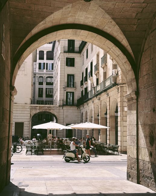 Cafe seating under archways in Alicante, Spain with a person on a scooter.