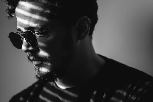 Free Black and white portrait of a man wearing round sunglasses with dramatic lighting and shadows. Stock Photo
