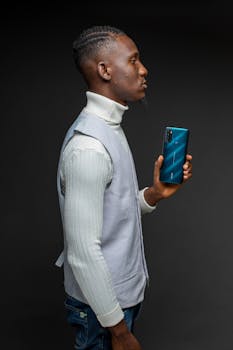 Sophisticated young man with smartphone posing in studio wearing vest and turtleneck.