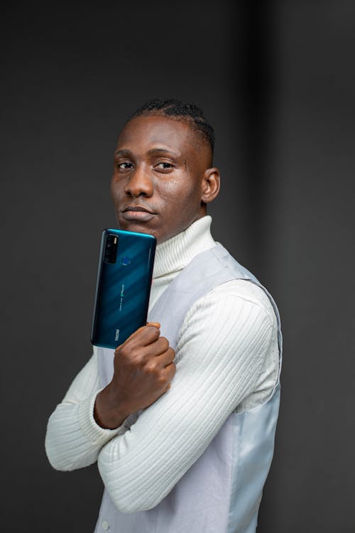 Man in White Turtleneck Sweater and Gray Vest Holding a Smart Phone