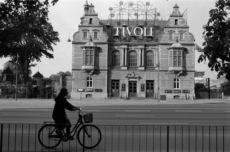 Woman On A Bicycle Passing By The Building Of Tivoli Gardens In Copenhagen, Denmark