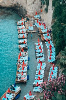 Peaceful seaside scene with lined sun loungers and red umbrellas beside turquoise waters, ideal for summer relaxation.