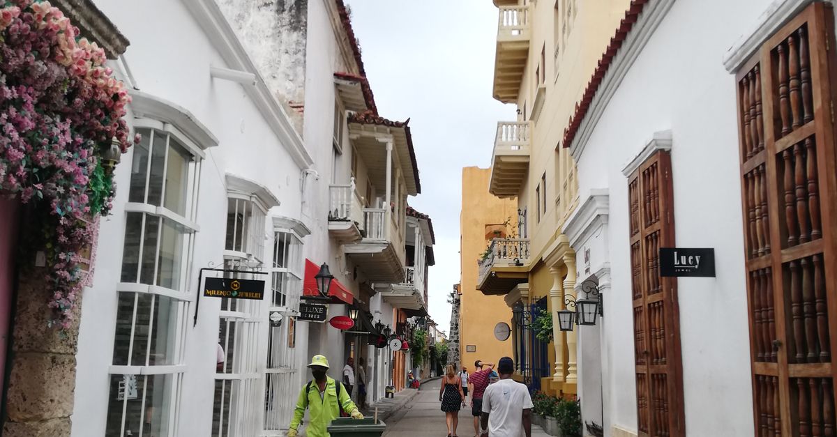Picturesque old town street with vibrant architecture and people walking amid street vendors and flowers.
