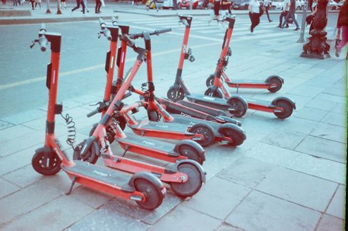 Free Red electric scooters lined up on an urban sidewalk with pedestrians in the background. Stock Photo