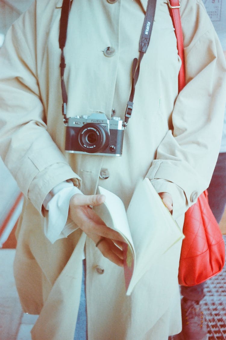 Person Walking In A White Coat Holding A Book, With A Camera