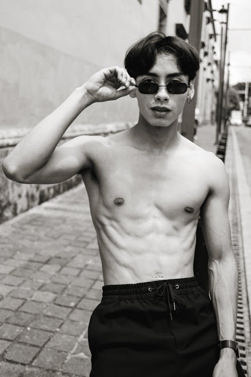Black and White Picture of a Shirtless Man in Sunglasses on the Sidewalk 