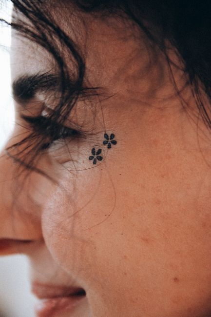 A close-up portrait of a woman with a floral tattoo near her eye, showcasing intricate details.