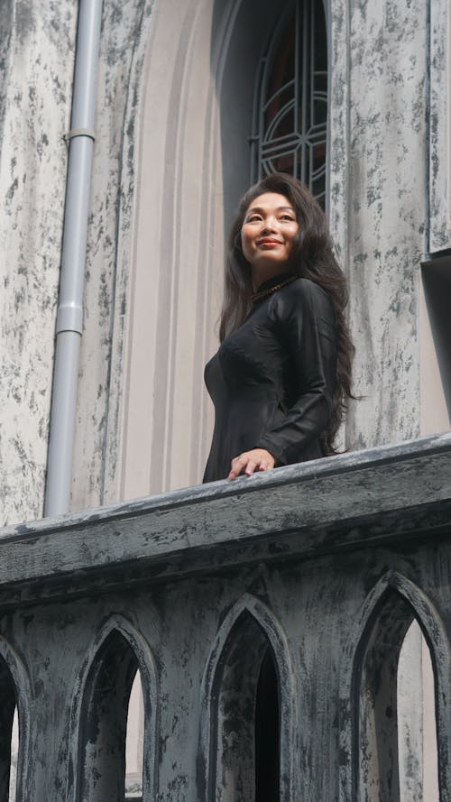 Young Woman Standing on the Balcony of a Gothic Building and Smiling 