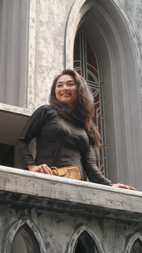 Young Woman Standing on the Balcony of a Gothic Building and Smiling 