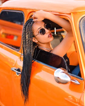 Woman with braids and sunglasses in a vintage orange car in Nairobi, capturing a retro vibe.