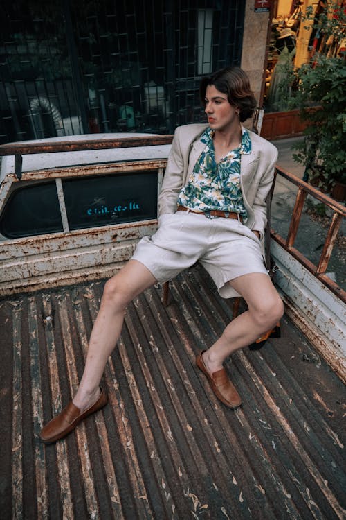 A Young Man in a Fashionable Outfit Sitting on the Back of a Rusty Truck 