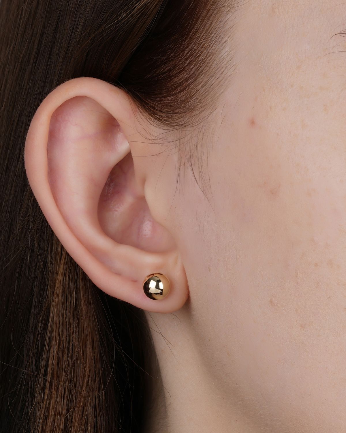 Close-up of a woman's ear wearing a small gold earring