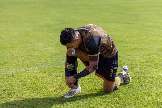 A soccer player kneels to tie shoelaces on a vibrant grassy field in Texcoco, Mexico.