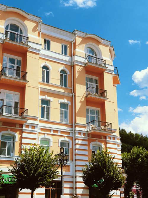 Free Charming yellow residential building with balconies and trees, set against a vibrant blue sky on a sunny day. Stock Photo