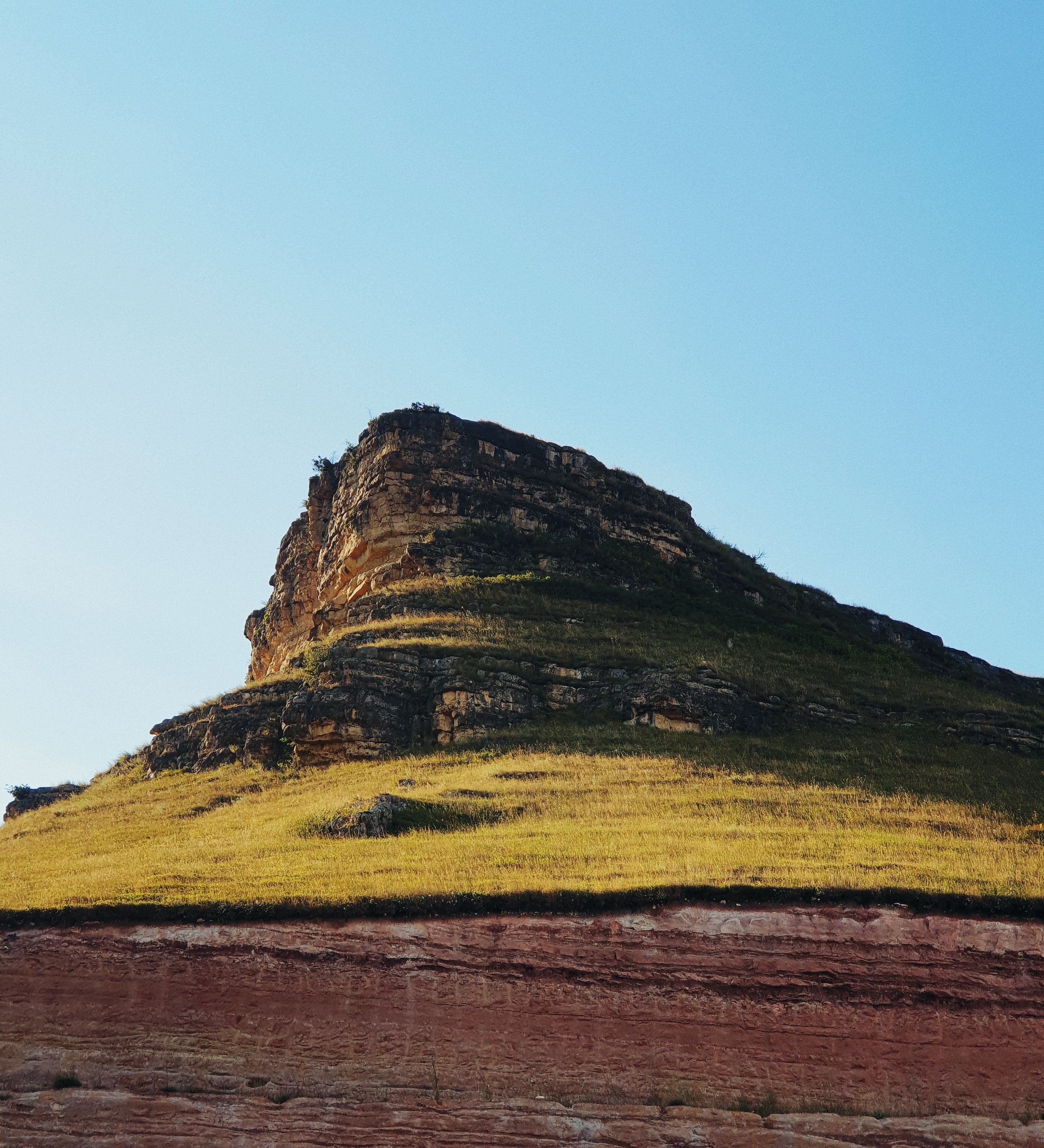 Scenic view of a sunlit hill with layered rock formations under a clear blue sky.