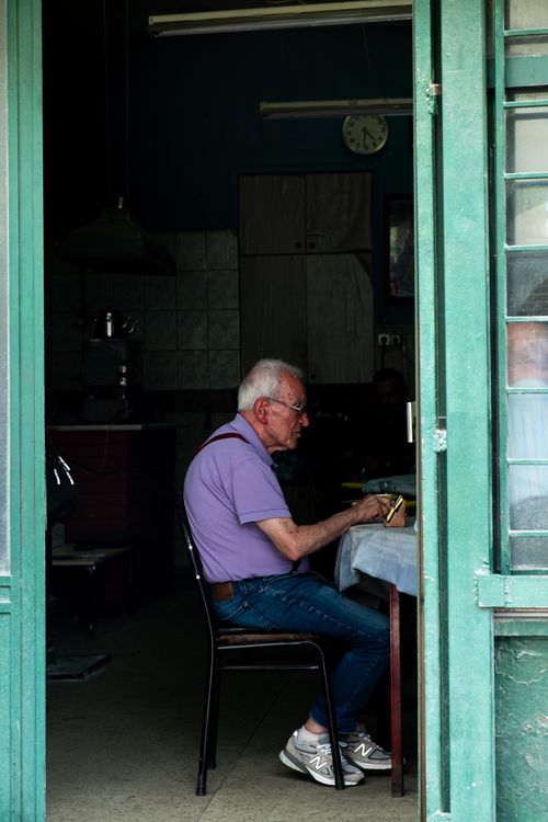 Free A senior man with gray hair sits at a table framed by a green doorway. Stock Photo