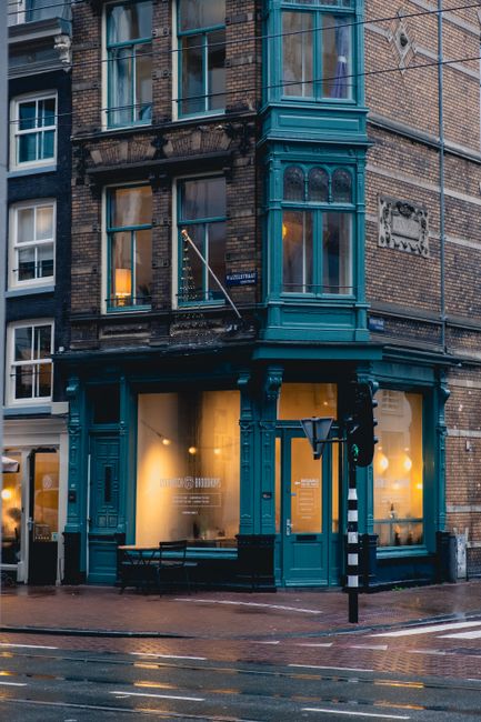 Street view of a charming brick café on a rainy day, with inviting lights glowing through large windows.