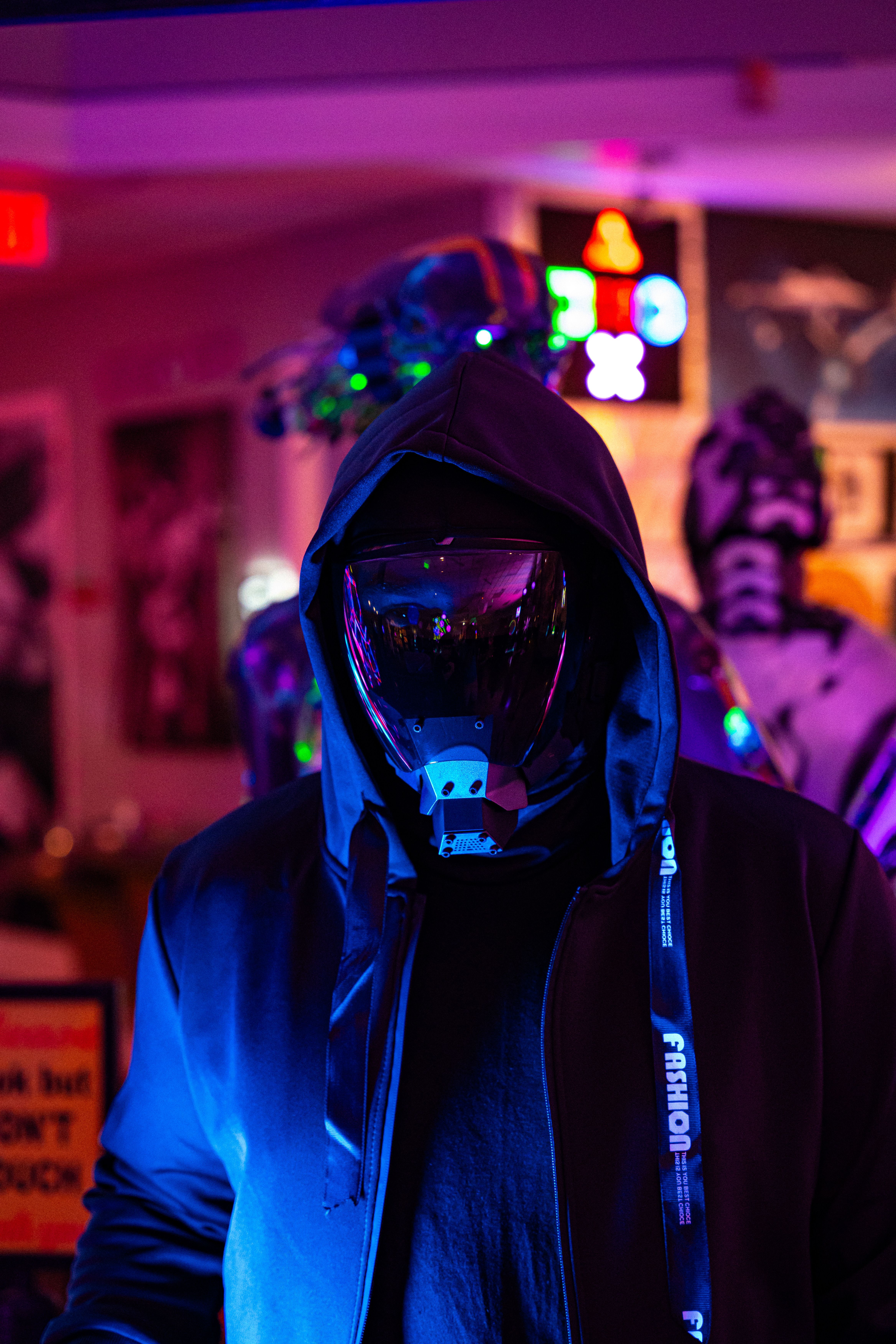 Person wearing a reflective mask under vibrant neon lighting indoors.