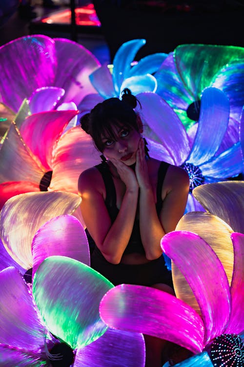 Young Woman Posing Between Colourful Fluorescent Luminous Flowers