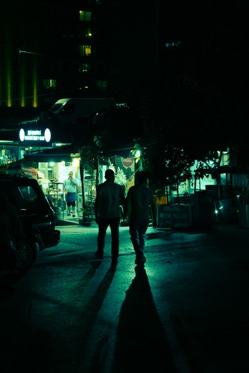 Free Two silhouetted figures walking at night in a city street, illuminated by store lights. Stock Photo