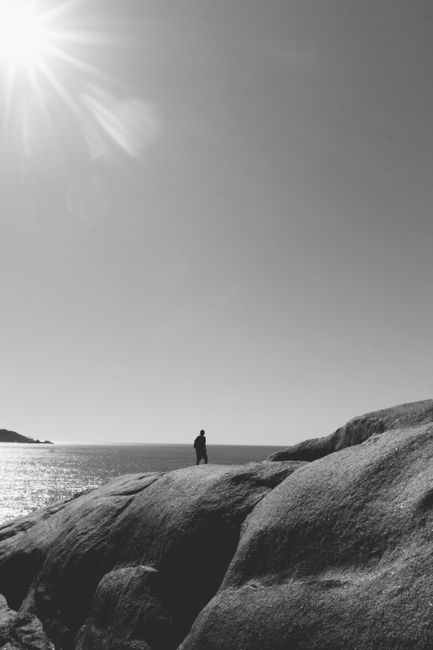 A man walking on sunlit rocks by the ocean in black and white, Florian贸polis, Brazil.