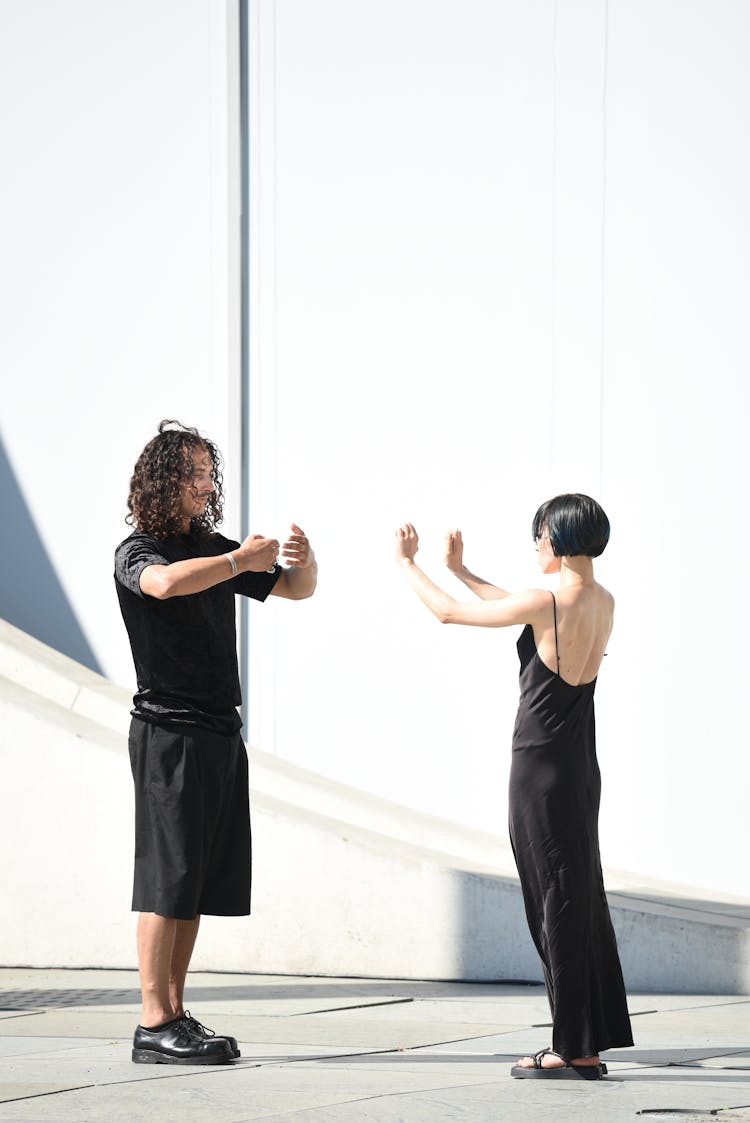 Side View Of A Man And A Woman Showing Hand Gestures To Each Other By A Building