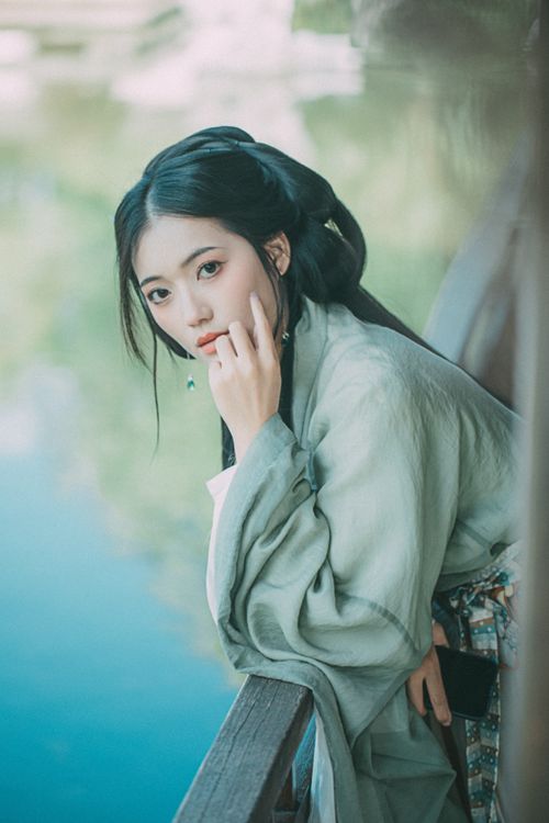 Free A woman in traditional attire poses gracefully by a picturesque pond against a wooden railing. Stock Photo