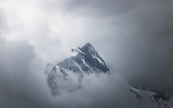 A stunning view of a snow-capped mountain peak enveloped in clouds, evoking adventure and serenity.