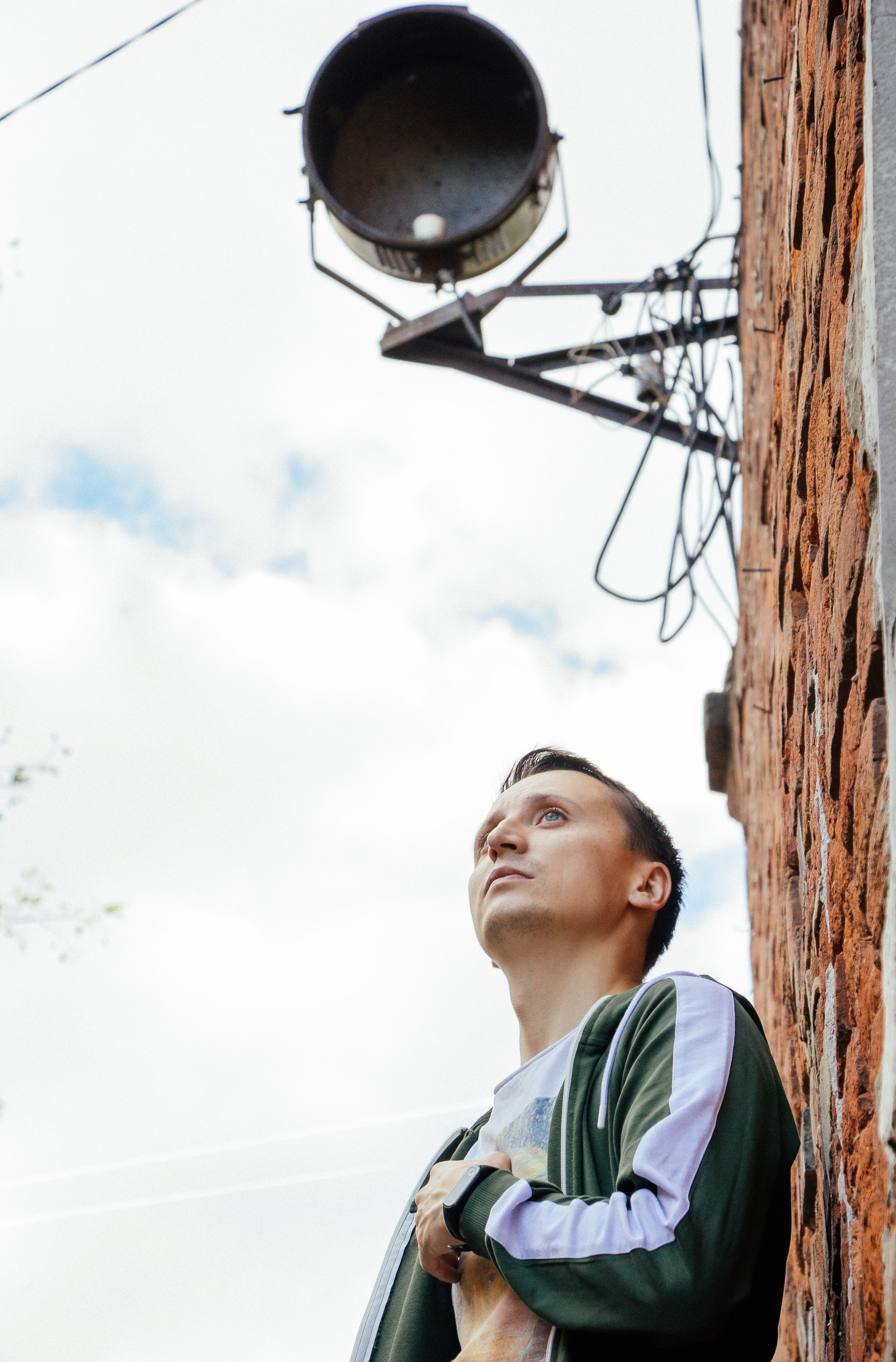 Man in tracksuit gazing upward against a brick wall and sky background.